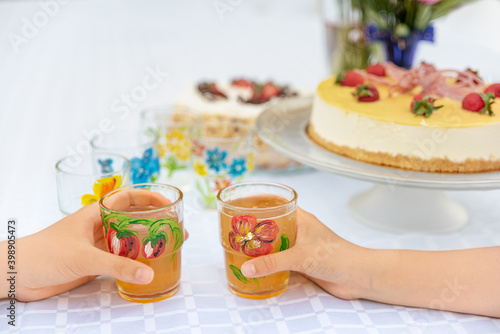 Birthday, party.  Children party. Cake on the table. Two kids hands holding glasses width juice.