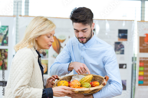 sales assistant showing basket of exotic fruits to mature customer