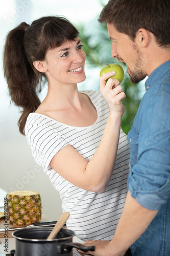 a wife feeding her husband an apple in their kitchen