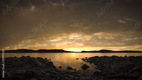 Peaceful lake scene at sunset or sunrise with a cloudy sky reflecting in the still water. A calm, tranquil and serene, natural landscape.   photo