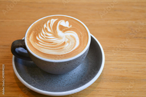 A hot latte cup with latte art on top put on wooden table.