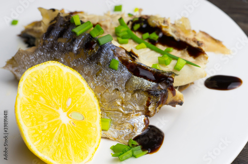 Grilled mackerel in a plate with herbs, lemon and sauce.