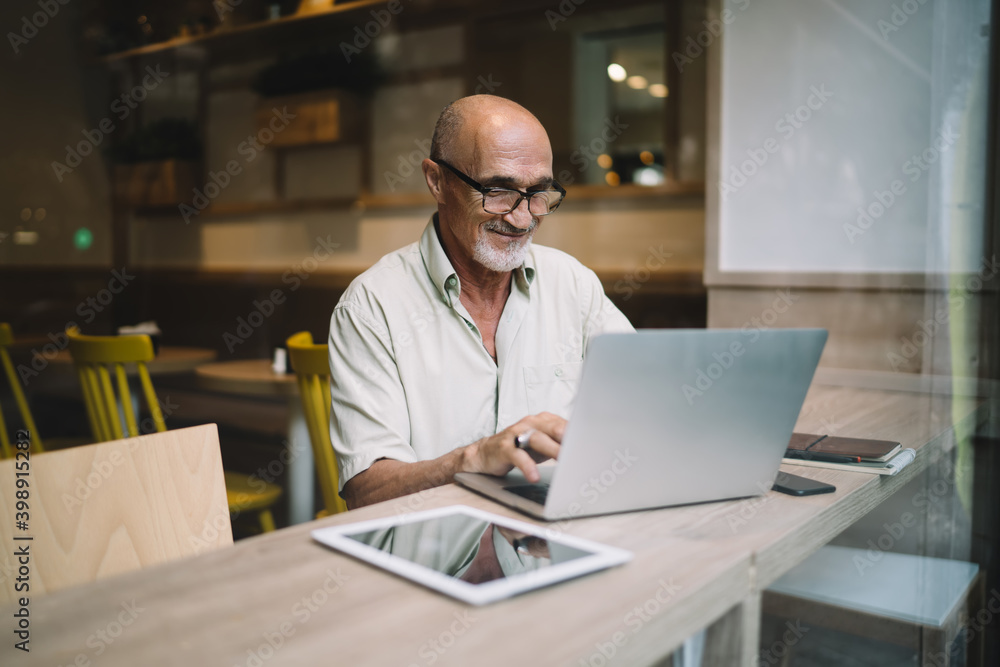 Mature Caucasian man in spectacles typing on laptop computer share content in blog browsing web pages and information, successful male freelancer doing remote job using netbook in coworking space Mature Caucasian man in spectacles typing on laptop computer share content in blog browsing web pages and information, successful male freelancer doing remote job using netbook in coworking space