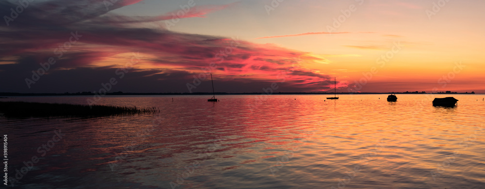Beautiful sunset with reflexion on calm sea with silhouettes of small boats - Panorama