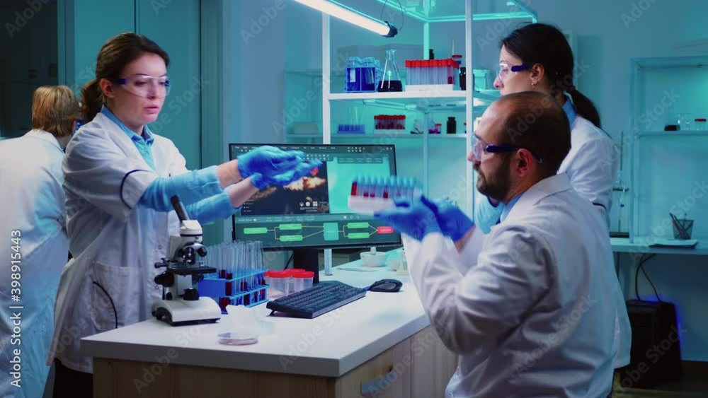 Microbiologist doctor taking a blood sample tube from rack with machines of analysis in the lab background. Doctors examining vaccine evolution using high tech researching diagnosis against covid19 Microbiologist doctor taking a blood sample tube from rack with machines of analysis in the lab background. Doctors examining vaccine evolution using high tech researching diagnosis against covid19