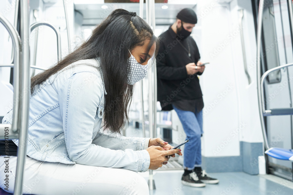 Obraz premium An African American girl and a Caucasian boy using the smartphone in the subway car. Young people in public transport abducted by technology.