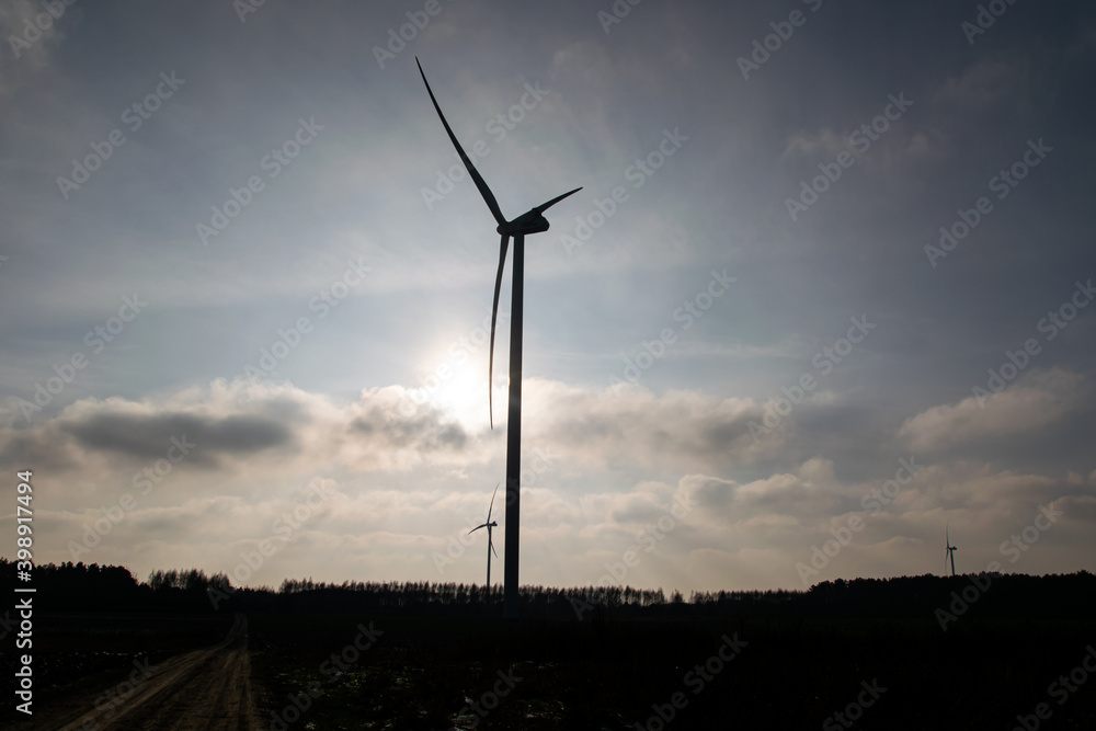Obraz premium Sunlight view of a giant wind turbine standing in the middle of a field against a blue sky with white clouds