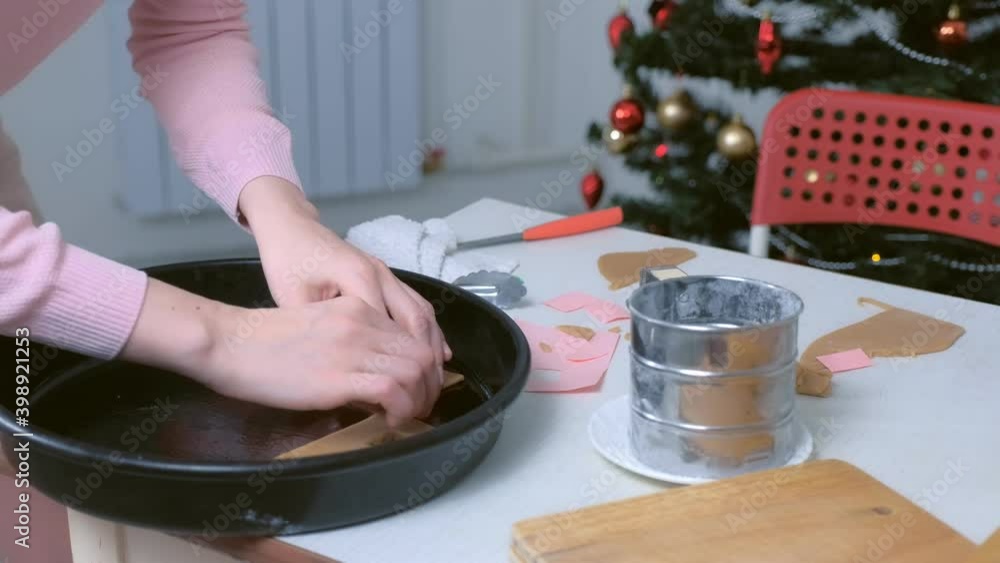Woman is putting parts of gingerbread house in baking tray, hands closeup. Cooking, baking cookies in New Year time. Sweet homemade bakery. Christmas preparation to holiday at home. Woman is putting parts of gingerbread house in baking tray, hands closeup. Cooking, baking cookies in New Year time. Sweet homemade bakery. Christmas preparation to holiday at home.