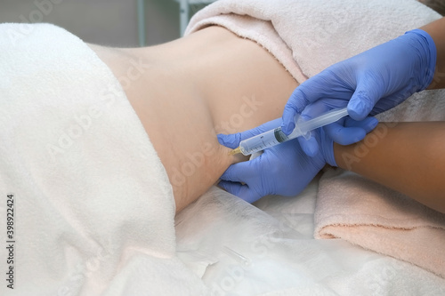 Doctor makes injection of ozone gas in patient abdomen on side on ozone therapy, closeup view. Treatment, cure and remove of skin tags and stretches. Cosmetologist woman in gloves. photo