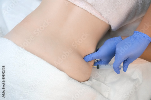 Doctor makes injection of ozone gas in patient abdomen on side on ozone therapy  closeup top view. Treatment  cure and remove of skin tags and stretches. Cosmetologist woman in gloves.