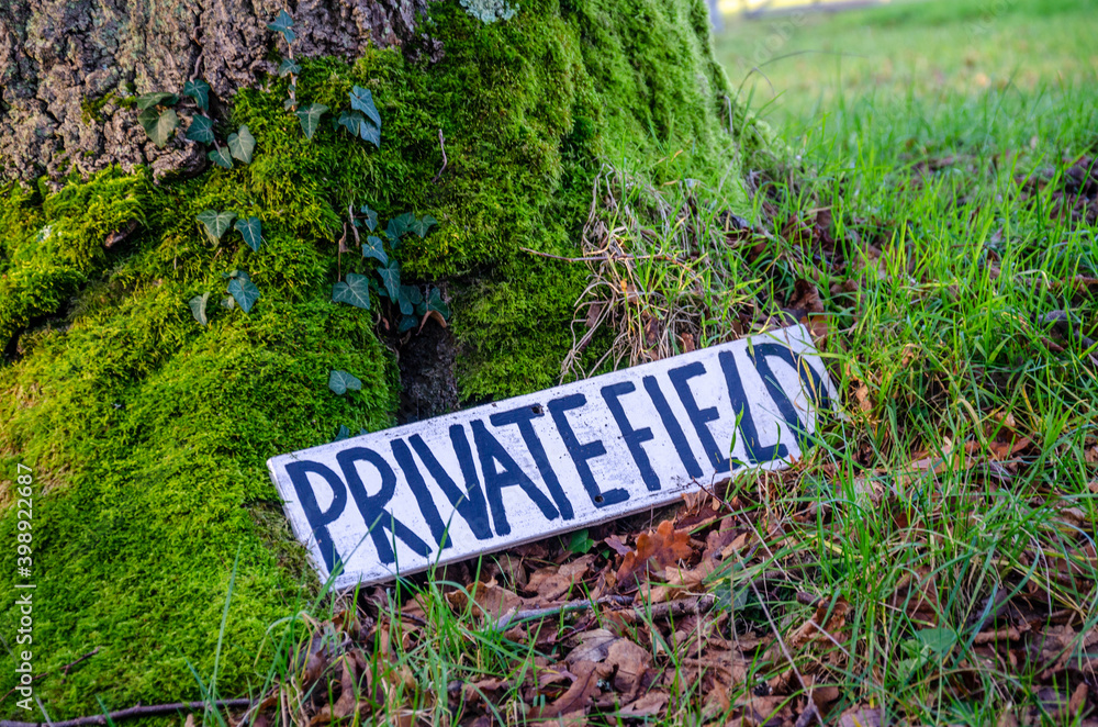 A sign at the base of a moss covered tree trunk starting that the field it is in is a private field