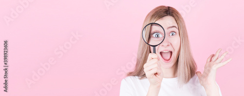 Young attractive blonde woman shocked while looking through a magnifying glass over pink background with copyspace.