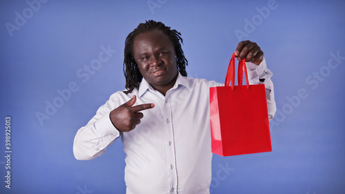 Young african american black man pointing finger on the red shopping bag. Presentig the gift. High quality photo photo