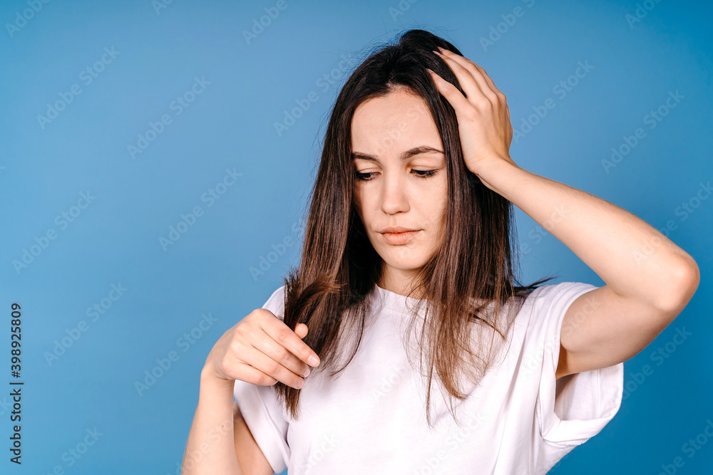 Portrait of upset girl with split ends hair isolated on blue