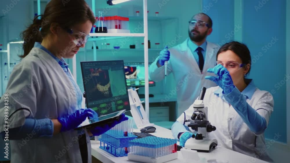 Team of positive scientists working in chemistry equipped laboratory, nurse typing on tablet. Group of doctors examining vaccine evolution using high tech researching diagnosis against covid19 virus Team of positive scientists working in chemistry equipped laboratory, nurse typing on tablet. Group of doctors examining vaccine evolution using high tech researching diagnosis against covid19 virus