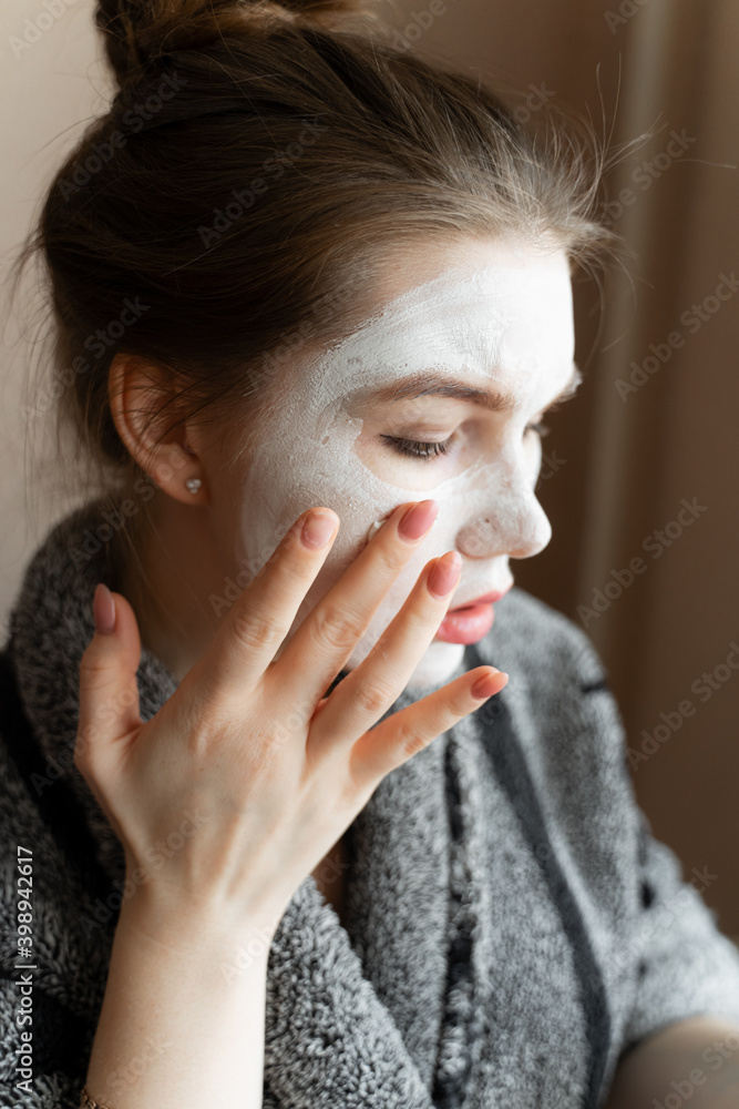 a girl takes care of the skin from the early morning, applies a white clay mask to her face, a woman in a gray terry cholat, spa procedures at home a girl takes care of the skin from the early morning, applies a white clay mask to her face, a woman in a gray terry cholat, spa procedures at home