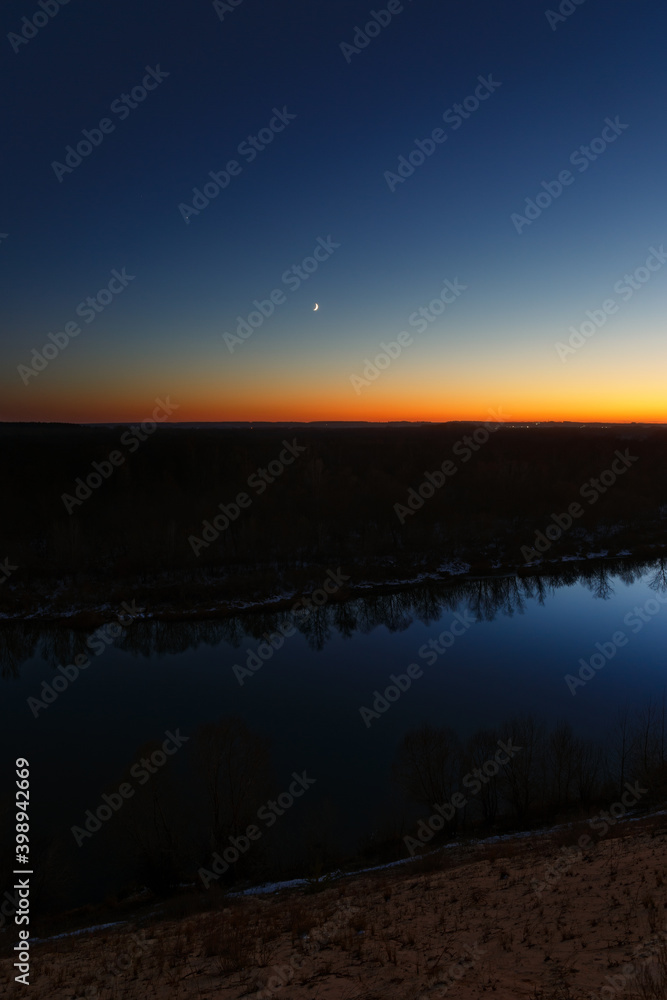 Obraz premium Young moon over the river at dusk. Bright evening sky after sunset.