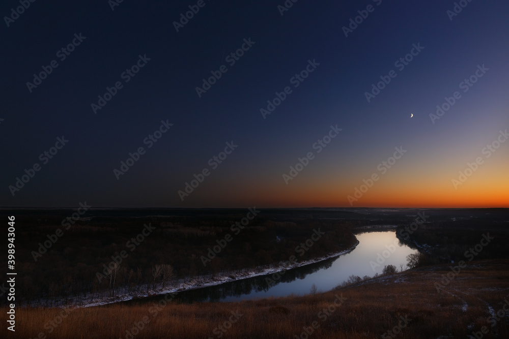 Fototapeta premium Young moon over the river at dusk. Bright evening sky after sunset.