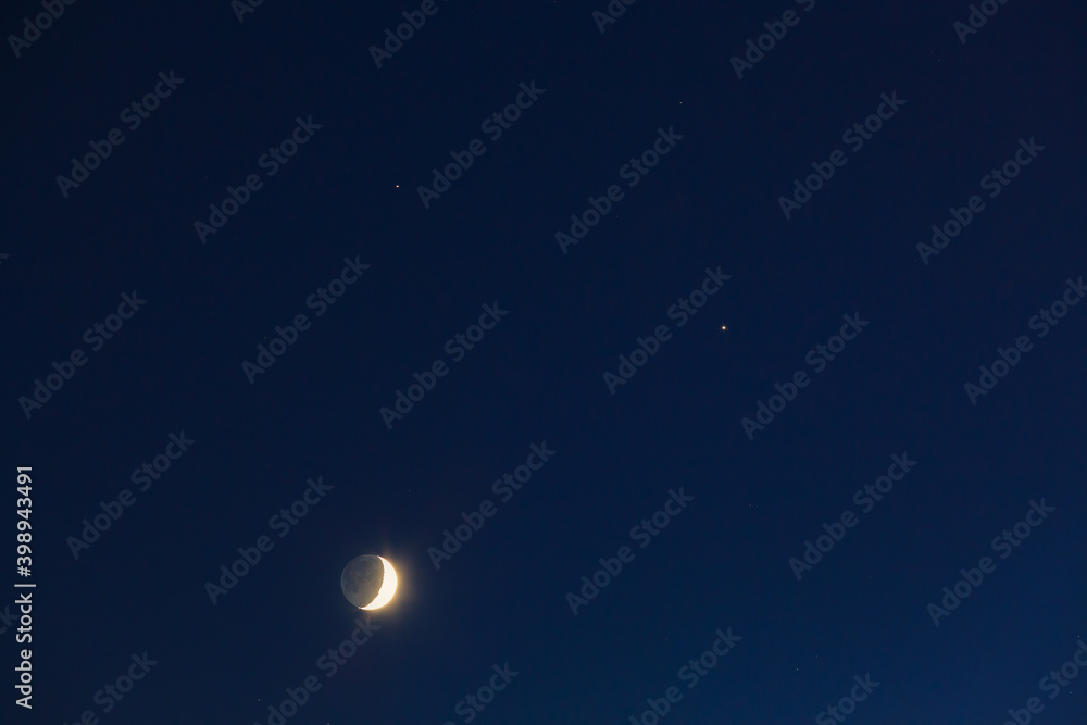 The conjunction of the Moon, Jupiter and Saturn in winter. Bright evening sky after sunset.