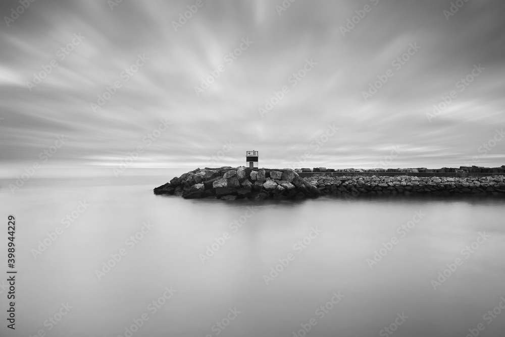 Fototapeta premium A concrete pier with a lighthouse at Oeiras Marina, Portugal. Long exposure fine art minimalistic black and white landscape.