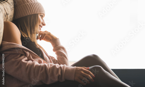 chica sentada al lado de una ventana con luz natural cálida, mientras mira a traves del cristal con mucha curiosidad.