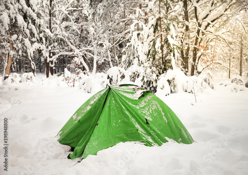 Green camping tent in snow at snowy winter wood