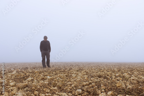 un hombre camina cabizbajo por un pedregal en la niebla. photo