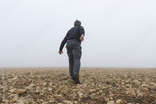 Hombre de espaldas se aleja por un pedregal hacia la niebla.

 photo