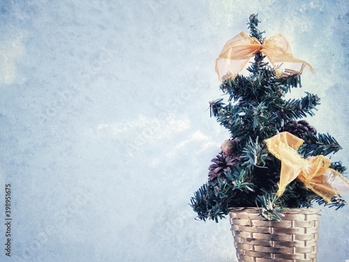 a small Christmas tree with orange bows and cones on a background of snow in a wicker basket