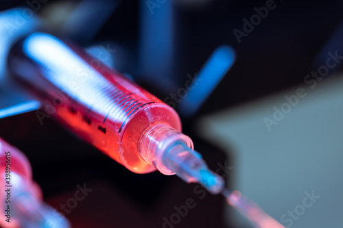 Pump pushing red liquid medium through syringes and flexible tubes in a small chip devise for an experiment in a scientific laboratory.