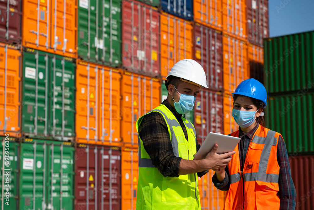Team of logistic engineer man and woman with medical face mask standing outside on a large commercial dock during pandemic Team of logistic engineer man and woman with medical face mask standing outside on a large commercial dock during pandemic