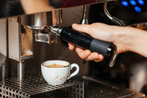 Barista's hand pours brewed fresh coffee from the coffee machine into a white cup. High quality photo