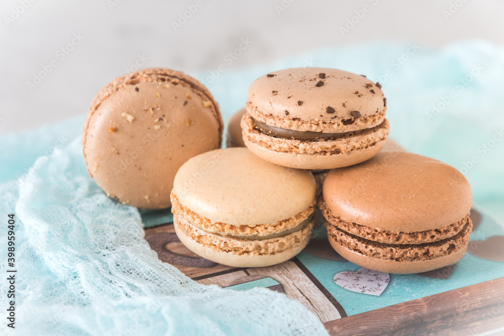 Four cream-colored and brown french macarons on a pretty metal tin