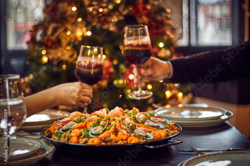 People sharing Spanish dinner table with assortment of dishes. paella, octopus, whole fish, sangría and wine. Dressed for christmas