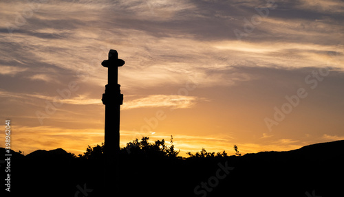 silhouette of stone cross backlit at sunset