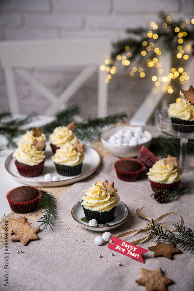 Chocolate and cherry cupcakes with mascarpone frosting and gingerbread cookies on festive table with bokeh lights on background.