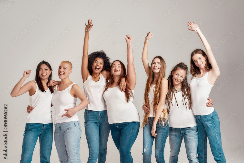 Group of beautiful diverse young women wearing white shirt and denim jeans  having fun, looking cheerful while posing together isolated over grey  background Stock Photo | Adobe Stock