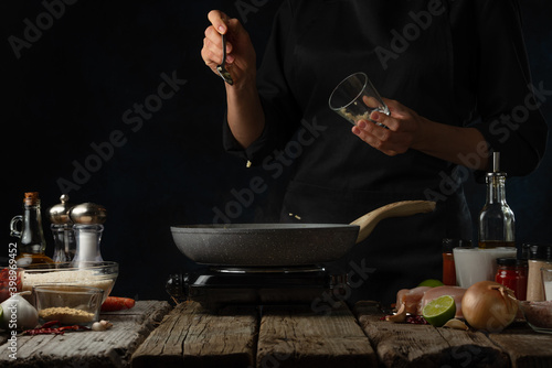 Wallpaper Mural Professional chef pours garlic into pan with frying chicken fillet. Backstage of cooking traditional Indian chicken curry on dark blue background. Frozen motion. Concept of cooking process. Torontodigital.ca