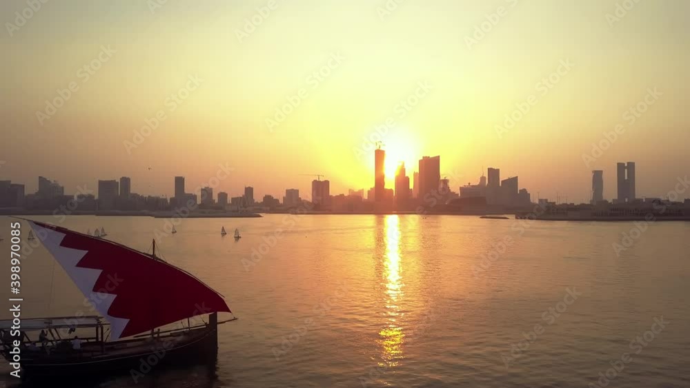 Drone view of the Traditional Arabic Dhow with Bahrain flag branded sails during the sunset time in front of Manama Skyline Drone view of the Traditional Arabic Dhow with Bahrain flag branded sails during the sunset time in front of Manama Skyline