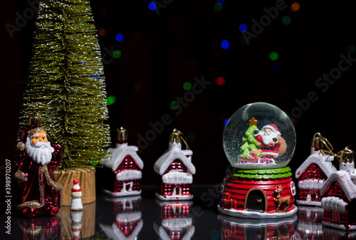 Santa Claus, Christmas tree and a snow globe on a dark, glossy table among toy houses.