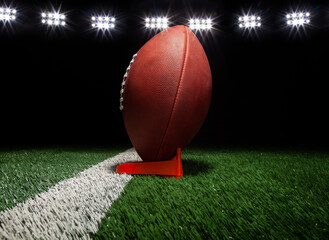 Low angle view of a football on a tee on black background under lights