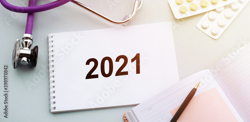 Stethoscope, pills and notebook with text 2021 on medical desk. 2021 medical vision