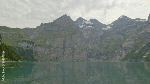 Time lapse panoramic view on a lake in mountains with snow spots and moving clouds. Oeschinnensee. Kandertal. Bernese Oberland. Canton Bern. Switzerland. photo