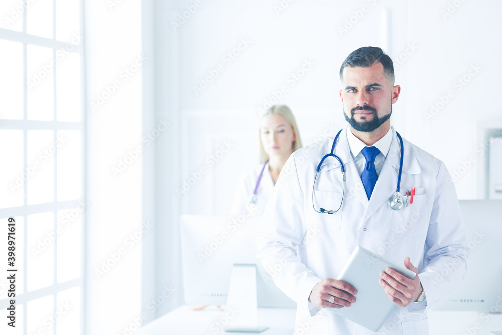 Confident smiling doctor posing and looking at camera with arms crossed, medical staff working on the background Confident smiling doctor posing and looking at camera with arms crossed, medical staff working on the background