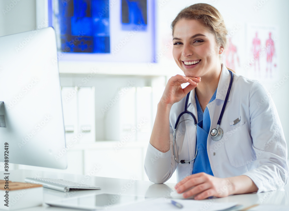 Young female doctor sitting at a desk and working on the computer at the hospital office. Health care, insurance and help concept. Physician ready to examine patient Young female doctor sitting at a desk and working on the computer at the hospital office. Health care, insurance and help concept. Physician ready to examine patient