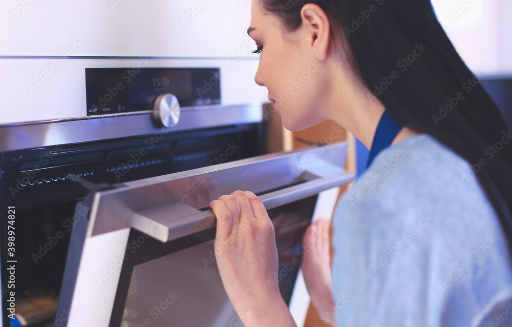 Beautiful young woman checking how her cake is doing in the oven Beautiful young woman checking how her cake is doing in the oven