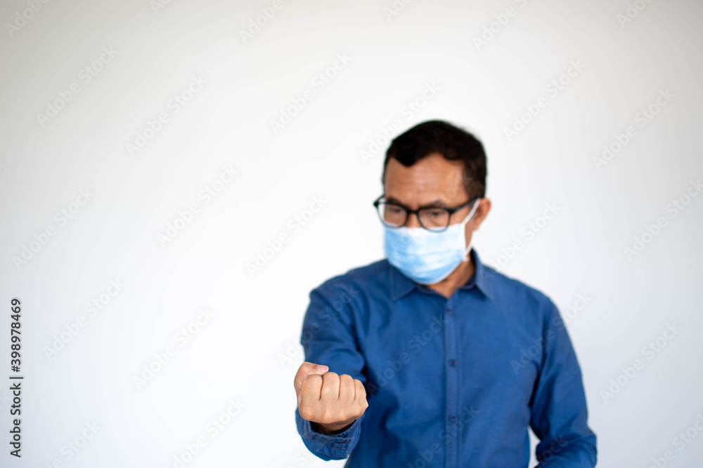 A young male is standing and fist clenched in anger. One man at home wearing a face mask to prevent coronavirus drainage or covid-19, Close up photo, and selective focus on hand. White background.