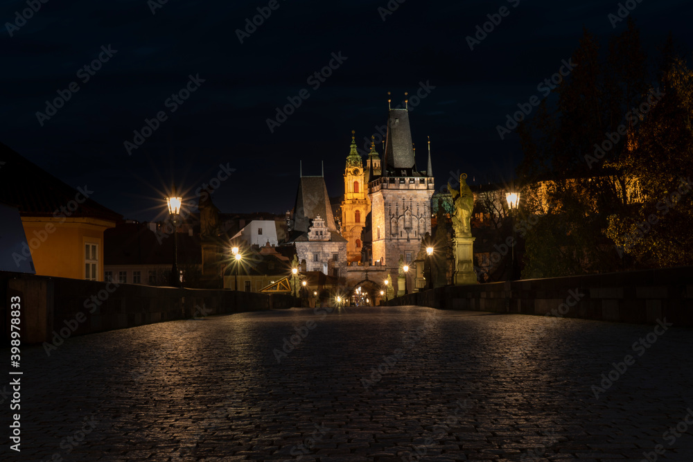 .old cobbled sidewalk with paving Charles Bridge in the center of Prague and in the background the old bridge tower at night in the Czech Republic and the light from street lighting