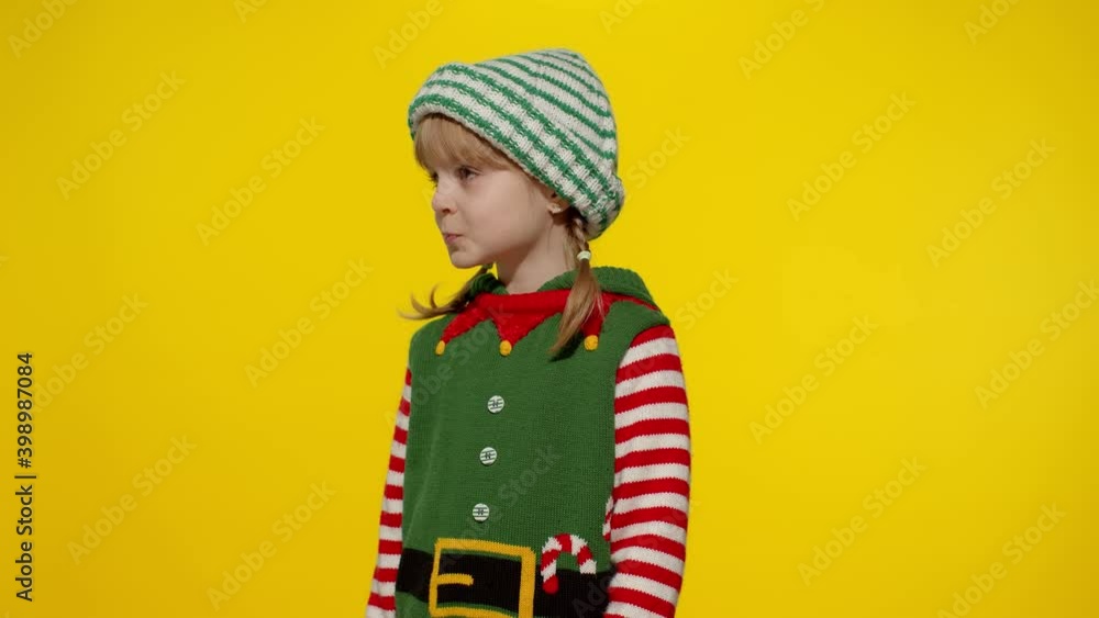 Displeased little blonde kid teen teenager girl in Christmas elf Santa helper costume isolated on yellow studio background. Child looking unhappily angry, sad at camera. Negative emotions and reaction Displeased little blonde kid teen teenager girl in Christmas elf Santa helper costume isolated on yellow studio background. Child looking unhappily angry, sad at camera. Negative emotions and reaction