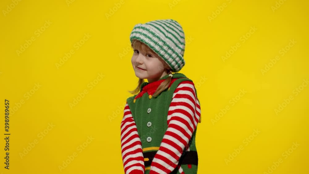 Shy shamed child girl in Christmas elf Santa helper costume posing looking camera smiling. Little kid feels guilty. Isolated on yellow background studio. People emotions. New Year holidays celebration Shy shamed child girl in Christmas elf Santa helper costume posing looking camera smiling. Little kid feels guilty. Isolated on yellow background studio. People emotions. New Year holidays celebration